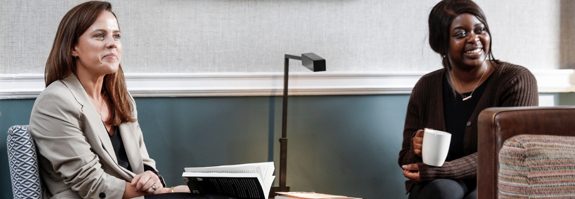 Two professional women listening to and smiling at another colleague outside of the frame